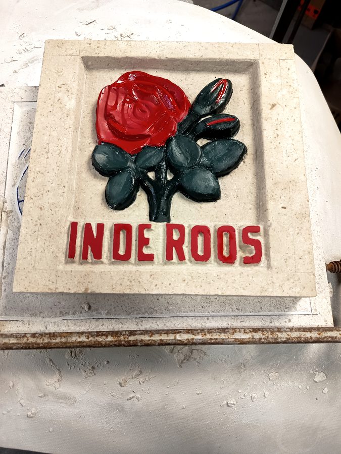 Handgehakte gevelsteen In de Roos met rode roos en bladwerk