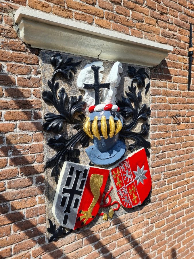 Gerestaureerde gevelsteen met wapenschilden aan een bakstenen gevel